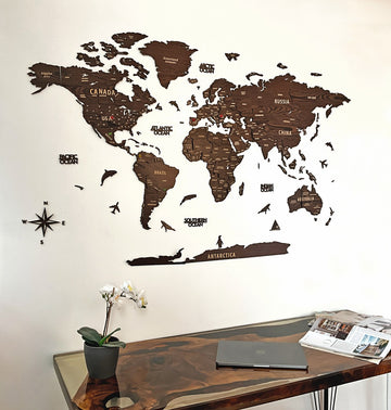 Dark brown wooden world map above a glass-top desk with an orchid, angled crop