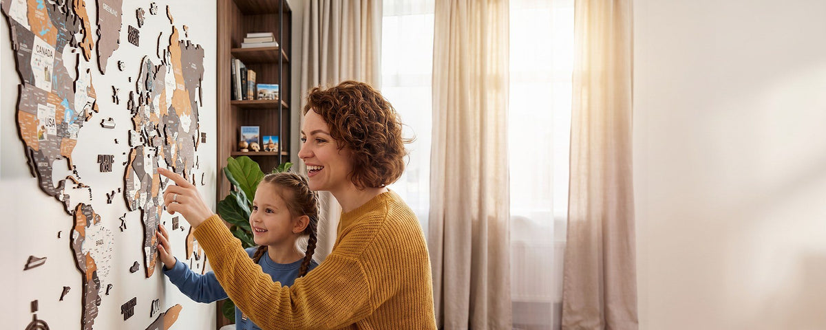 Mother and daughter pointing at countries on a colorful wooden world map on the living room wall