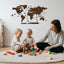 A woman and two children play with toys in a room with a wooden world map on the wall