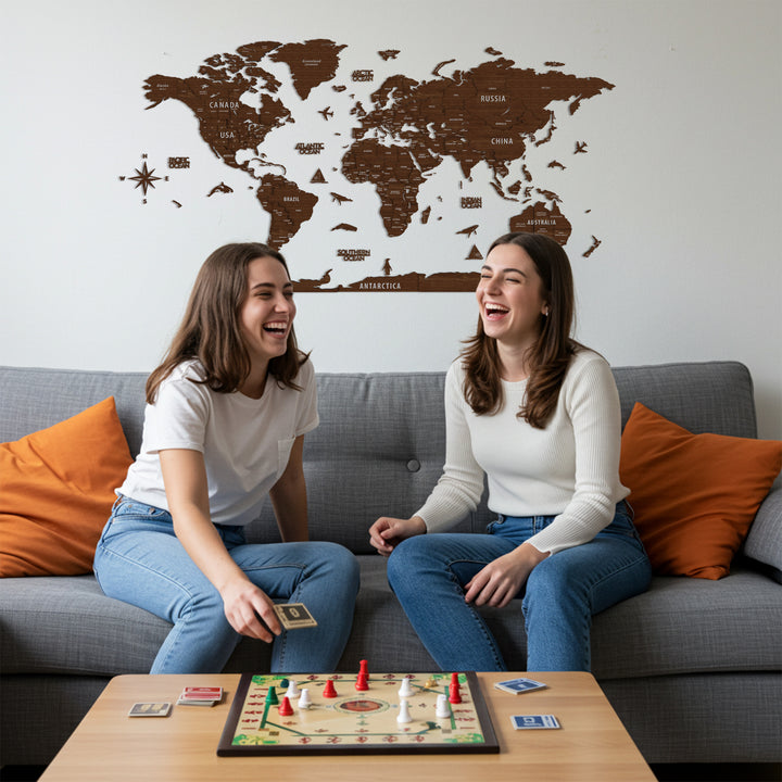 Two women sitting on a couch playing a board game with a world map in the background.