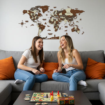 Multicolor wooden world map above a gray sofa where two friends sit laughing