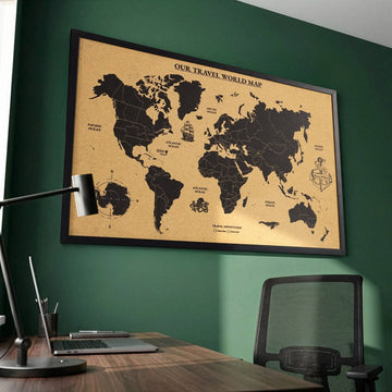 Black framed cork world map on a green wall, angled view over a desk with a laptop