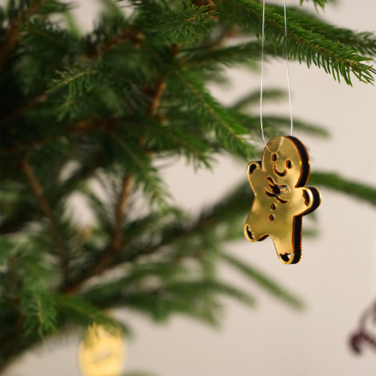 Gold mirror acrylic gingerbread man Christmas ornament hanging from a fir branch on a thin string