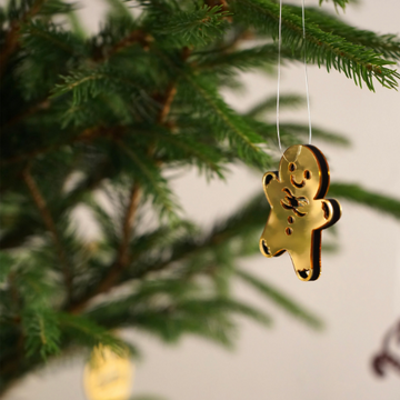 Gold mirror acrylic gingerbread man Christmas ornament hanging from a fir branch on a thin string