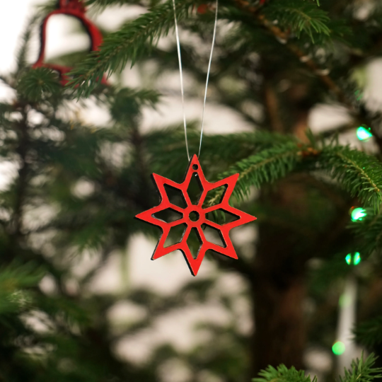 Red wooden snowflake Christmas ornament hanging on a thin string in a Christmas tree