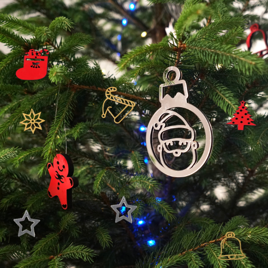 Wooden and acrylic Christmas ornaments on a fir tree, with a silver Santa bauble, a red gingerbread man and gold pieces