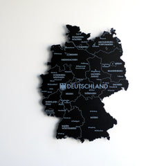 Black UV printed metal Germany map with state and city names, front view on a white wall