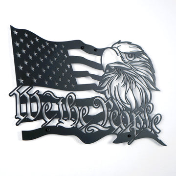 Black We The People metal wall art with flag stripes and eagle, angled view on a white wall