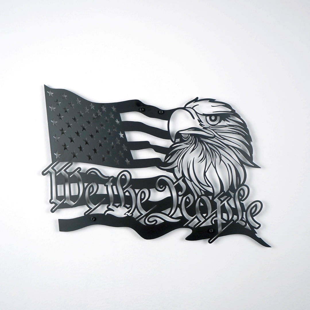 Black We The People US flag metal wall decor on a white wall, front view with eagle head