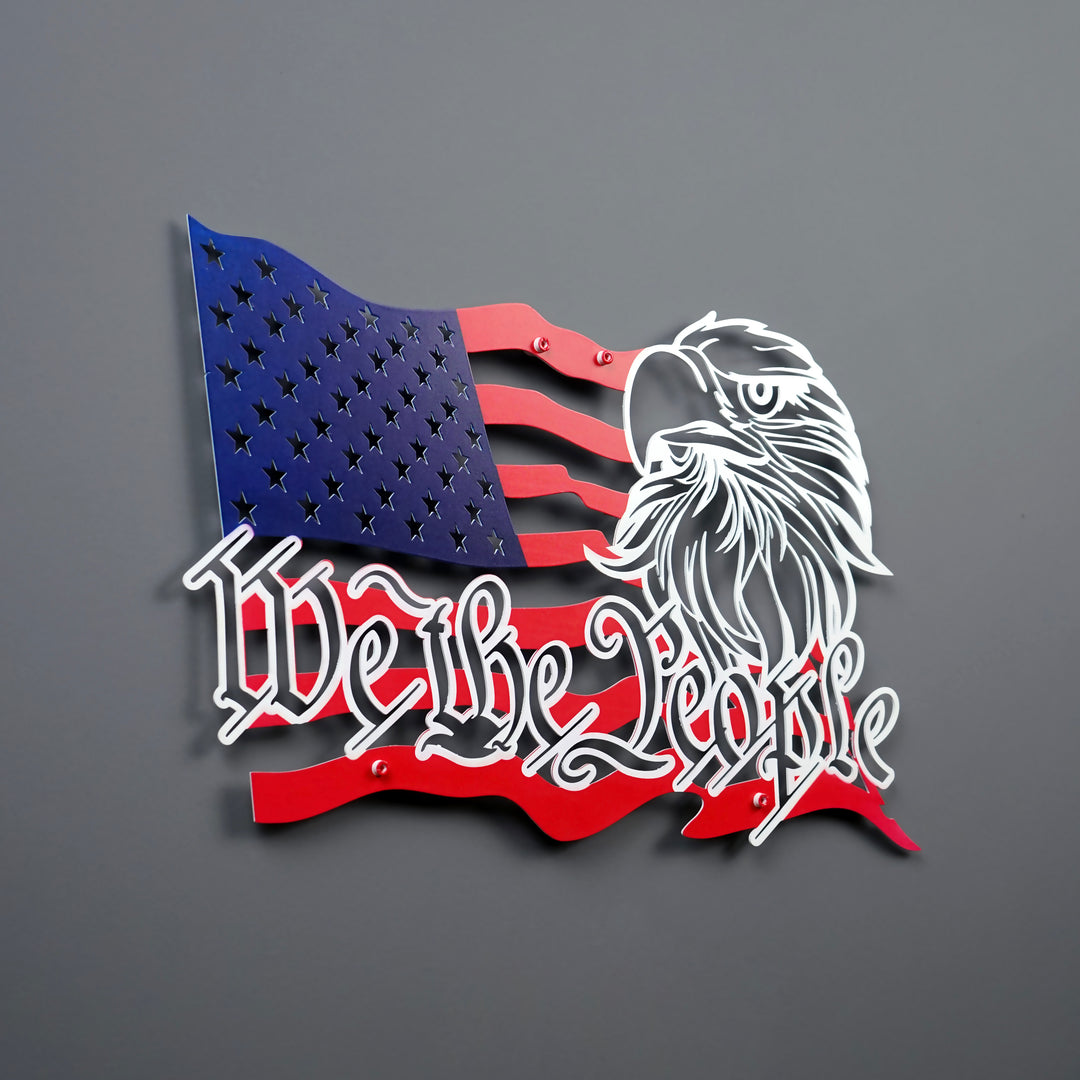 We The People US flag metal wall decor in red, blue and white, angled from the left on a gray wall